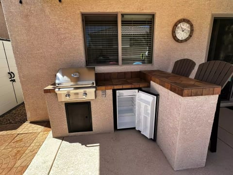 Outdoor kitchen area with a professional BBQ, fridge, and 2 bar stools