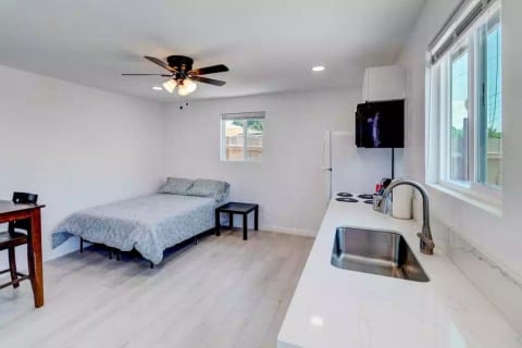 Open Studio Layout with Full Size (Double) Bed, Mounted 55" Roku TV, Full Fridge/Freezer, Mini 24" Range Stovetop w/ Oven, Microwave, and Dining Table w/ Chairs.